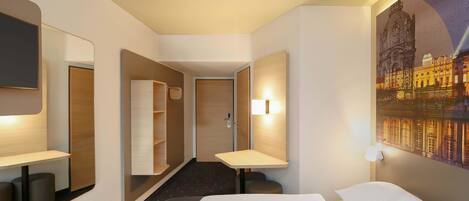 Une chambre d’hôtel comprenant un lit, un bureau, un miroir, une armoire et un tableau représentant un paysage urbain.