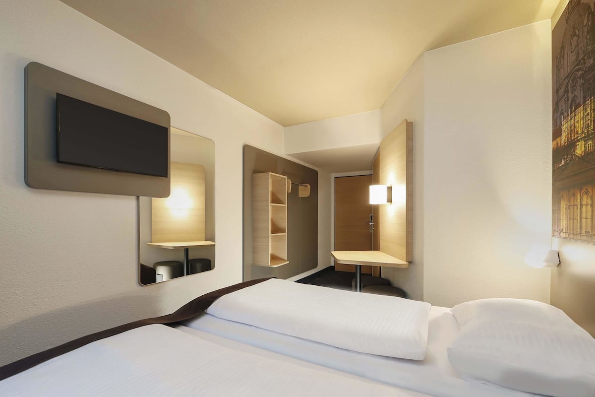 Habitació d'hotel amb un llit, un televisor fixat a la paret, un mirall i una taula petita.