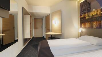 Ein Hotelzimmer mit einem Bett, einem Schreibtisch, einem Stuhl, einem Spiegel, einer Tür und einer Wandleuchte.
