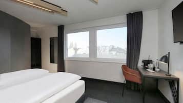 Una habitación de hotel con cama, escritorio con silla, televisión y ventana con cortinas.