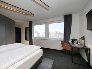 A hotel room with a bed, a desk with a chair, a TV, and a window with curtains. - B&B Hotel Berlin City-West (Berlin)