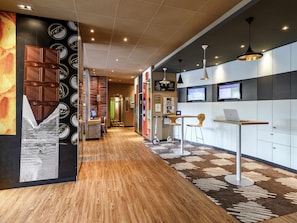 A modern hotel lobby with a reception desk, seating area, and a digital screen displaying information. - ibis Winterthur City (Winterthur)
