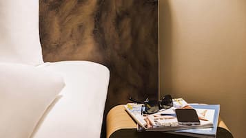 A neatly made bed with white linens, a wooden headboard, and a bedside table with a magazine, a pair of glasses, and a smartphone.