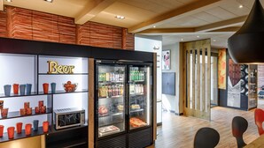 Un interior moderno con una cafetería, un expositor refrigerado y una zona de estar con suelo de madera.