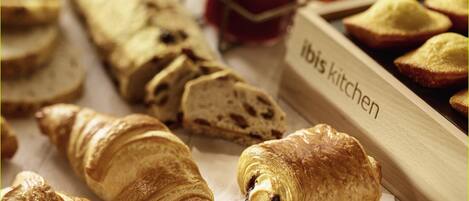 A variety of pastries and bread, including croissants and a baguette, displayed on a table with a label that reads 'ibis kitchen'.
