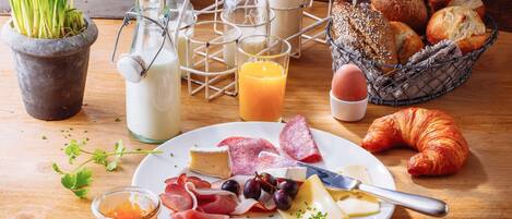 A breakfast setting with a plate of cheese, meats, and bread, a glass of orange juice, and a croissant.