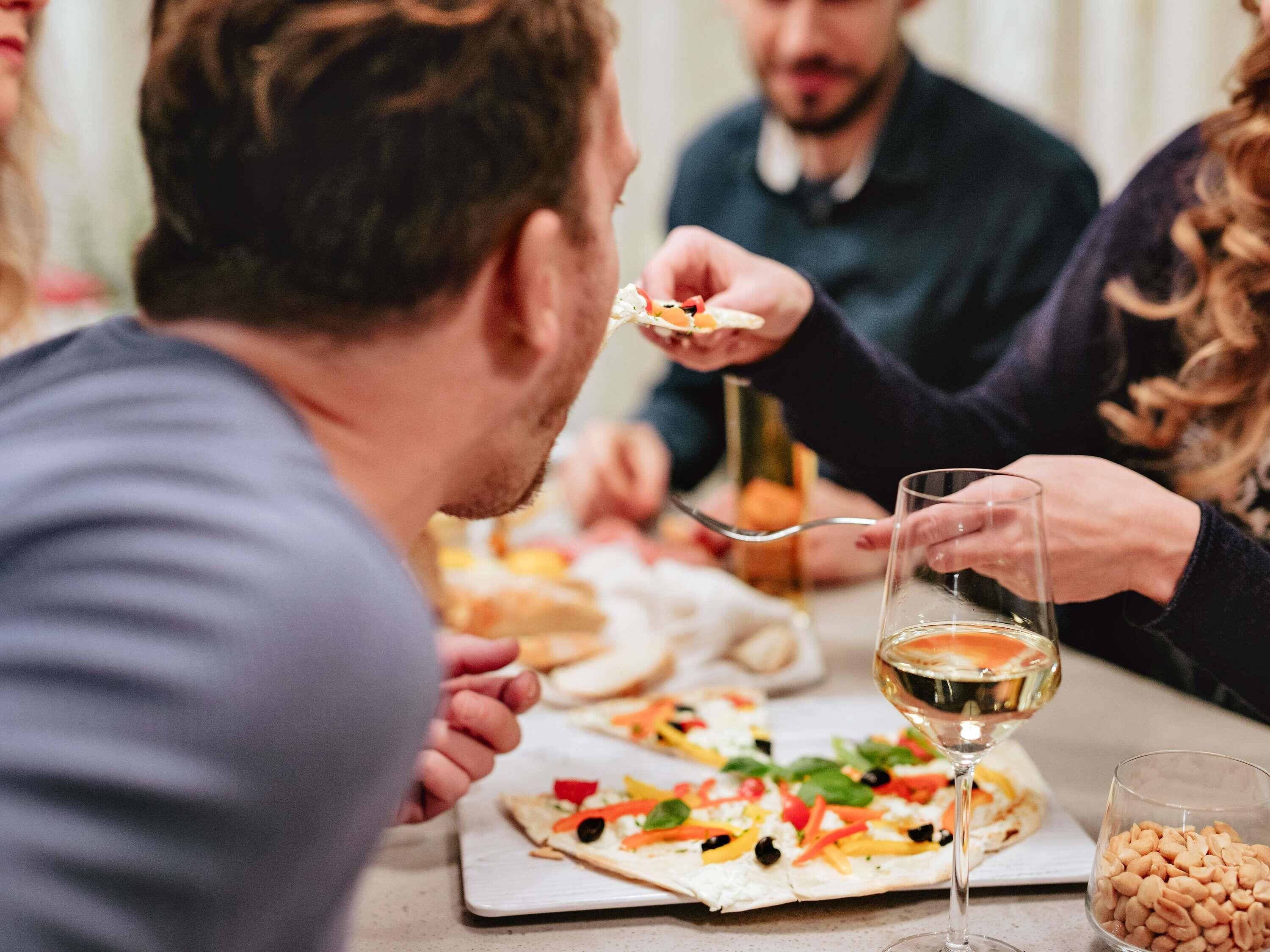 A group of people dining at a table with pizza and a glass of wine.