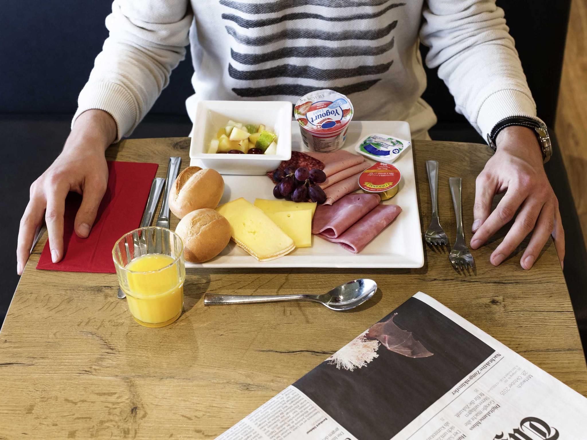 A meal tray with cheese, ham, grapes, and a yogurt container on a wooden table.
