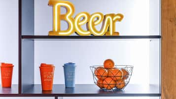 Una estantería con un letrero de neón que dice 'Beer', dos vasos anaranjados, un vaso azul y una cesta de naranjas.