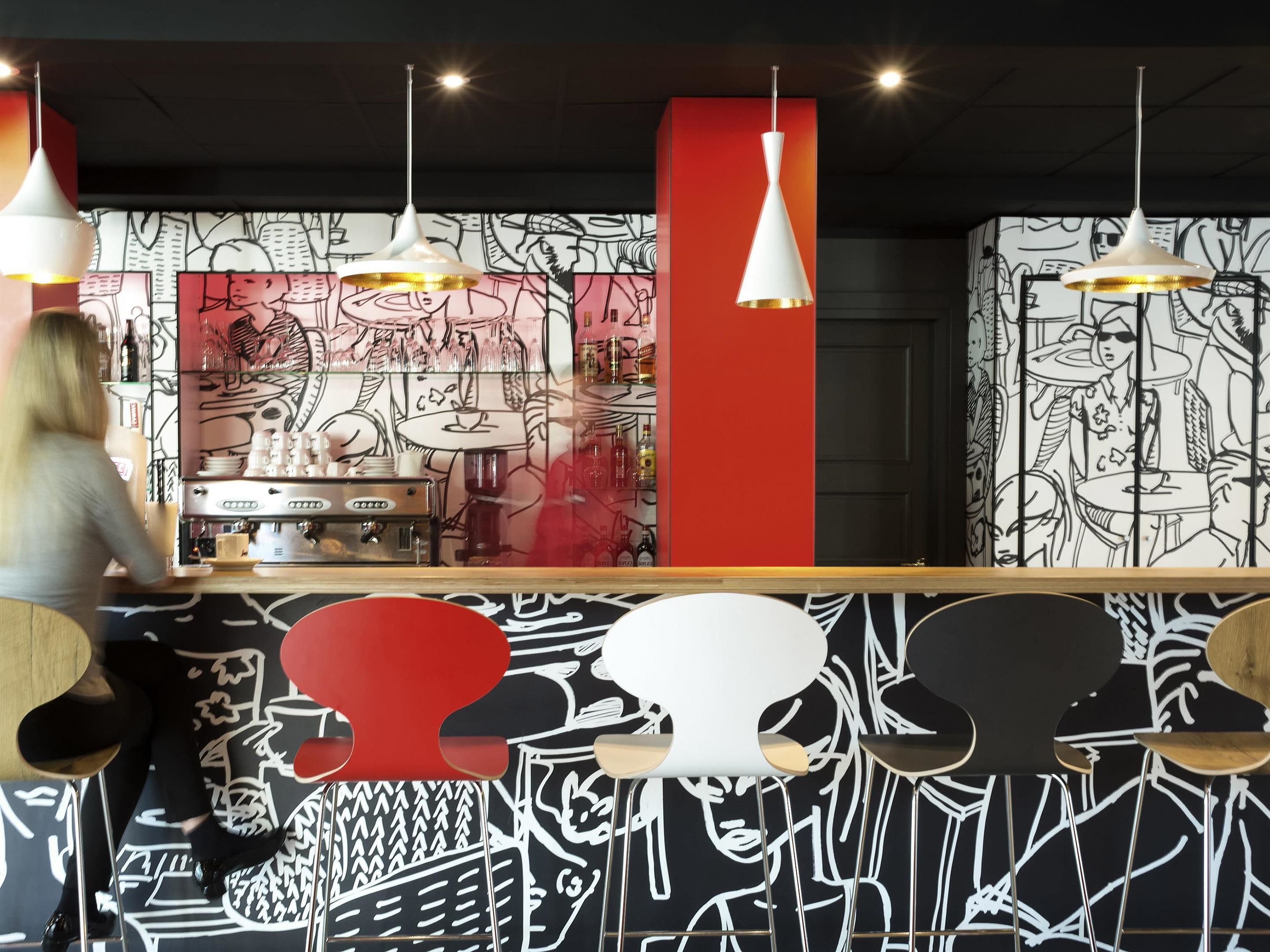 Een bar met een toonbank, hangende lampen en een muur met zwart-wit kunst.