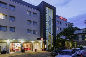Un hotel moderno con una fachada de vidrio destacada, una escalera visible y un estacionamiento con varios automóviles.