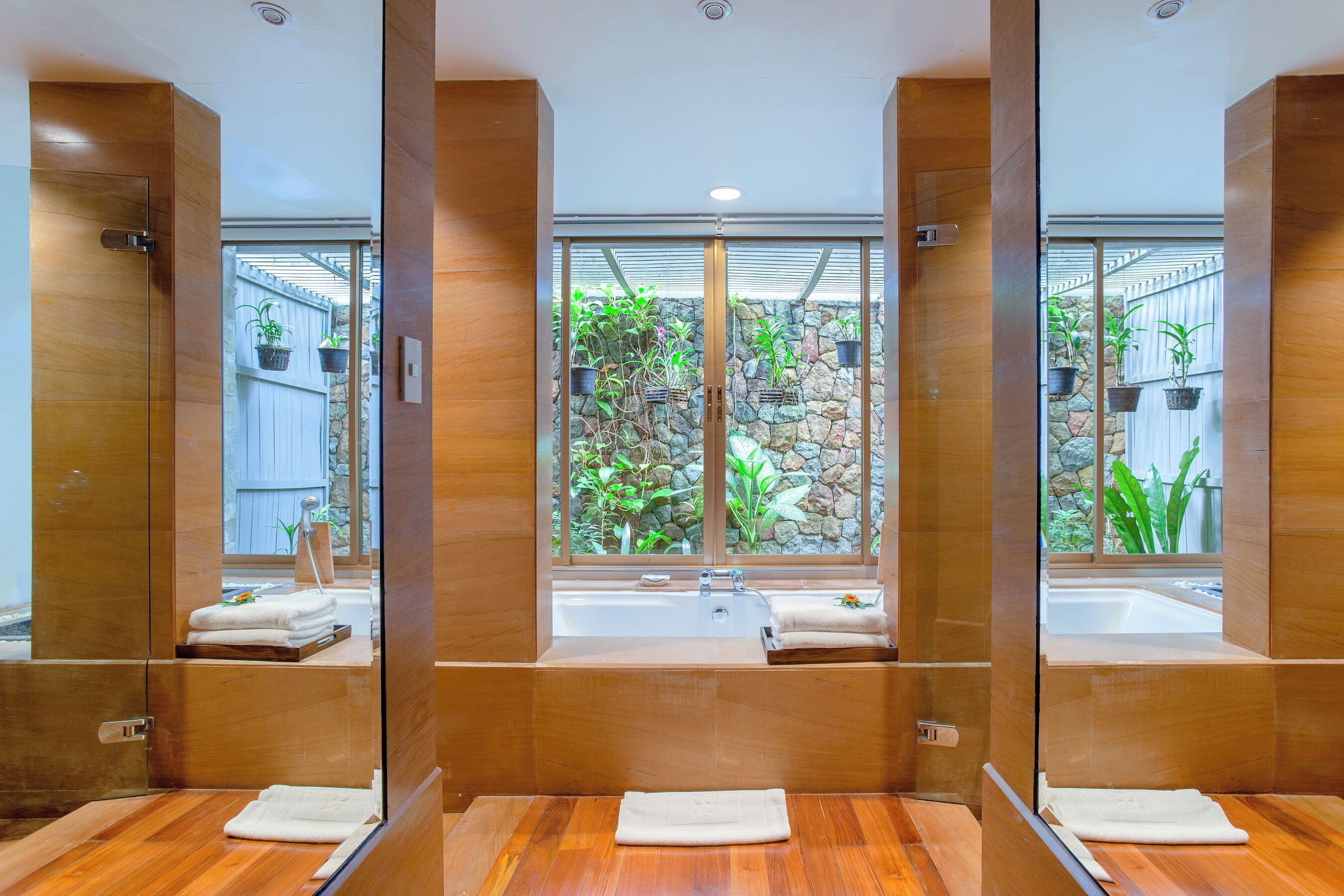 Un baño moderno con un espejo grande, tocador de madera y una bañera con vista a una pared de piedra.