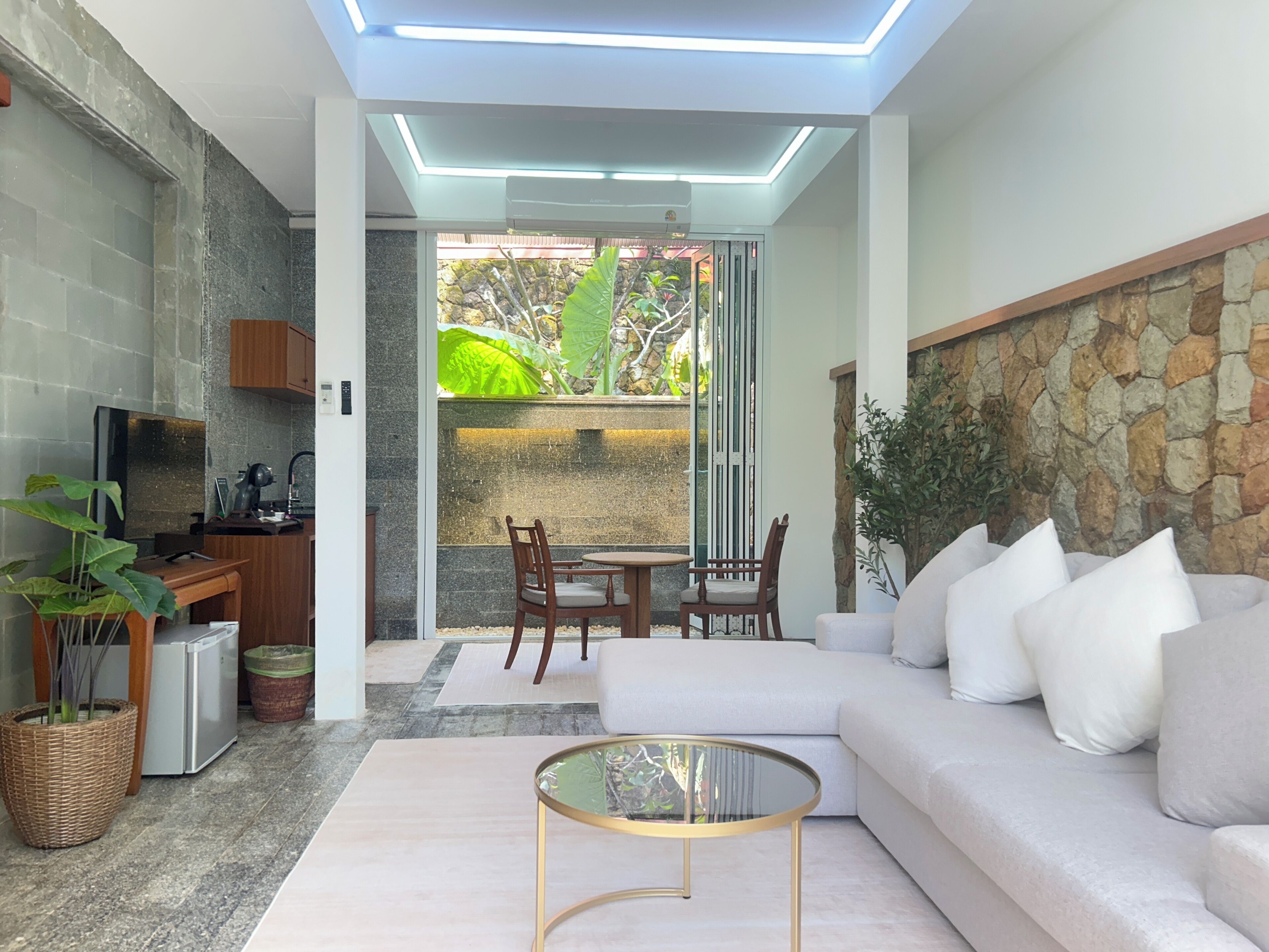A modern living room with a sofa, a glass coffee table, a TV, and a kitchen area with a refrigerator.