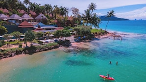 Un resort costero con bungalows sobre el agua, una playa y aguas turquesas cristalinas.