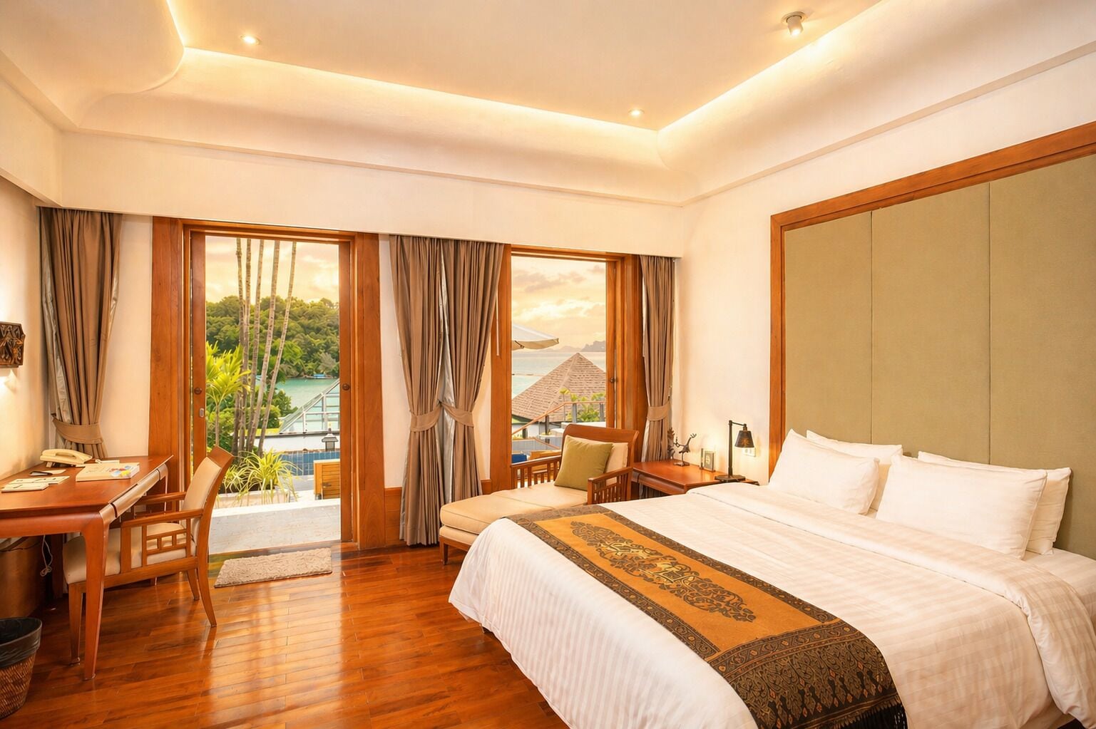 A hotel room with a large bed, a desk, a chair, and a view of a tropical landscape.