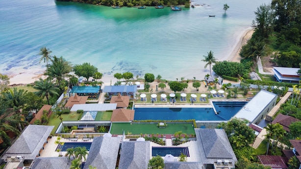 Vista aérea de un resort con piscina, playa y barcos en el agua.