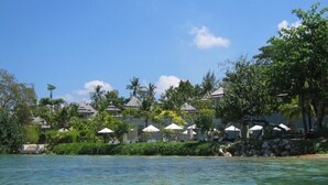 Un resort frente al mar con bungalows sobre el agua, aguas azules cristalinas y exuberante vegetación.