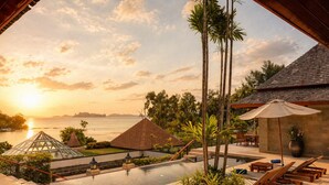 Piscina de resort con sillones de descanso, un pabellón y vista al atardecer sobre el agua.