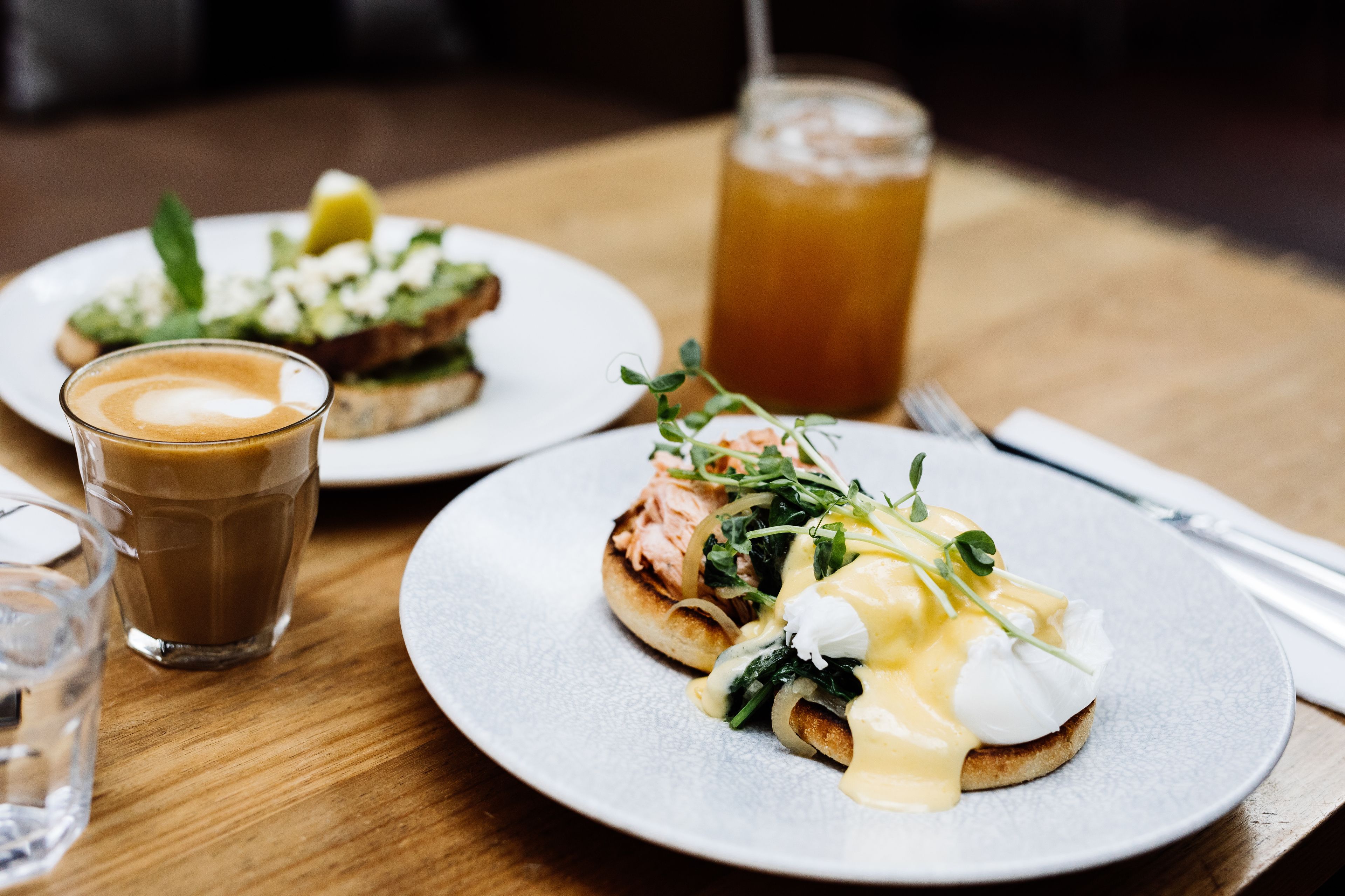 A breakfast setting with two plates of food, a glass of coffee, and a glass of iced tea on a wooden table.