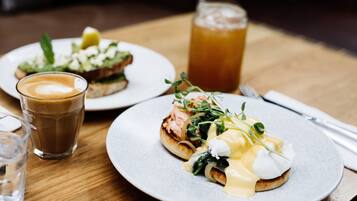A breakfast setting with two plates of food, a glass of coffee, and a glass of iced tea on a wooden table.