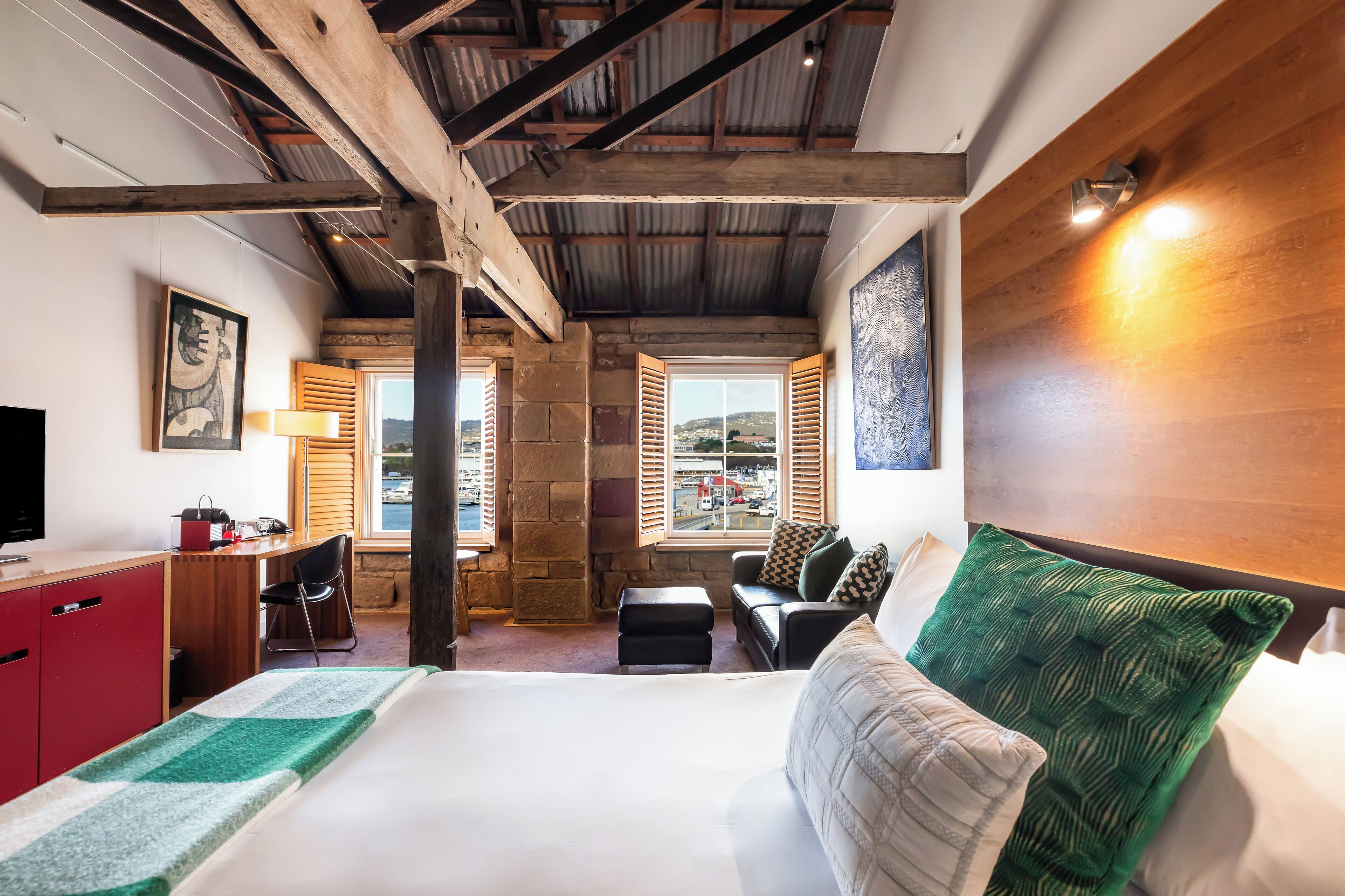 A hotel room with a bed, a desk, a chair, a small table, and a window with shutters.