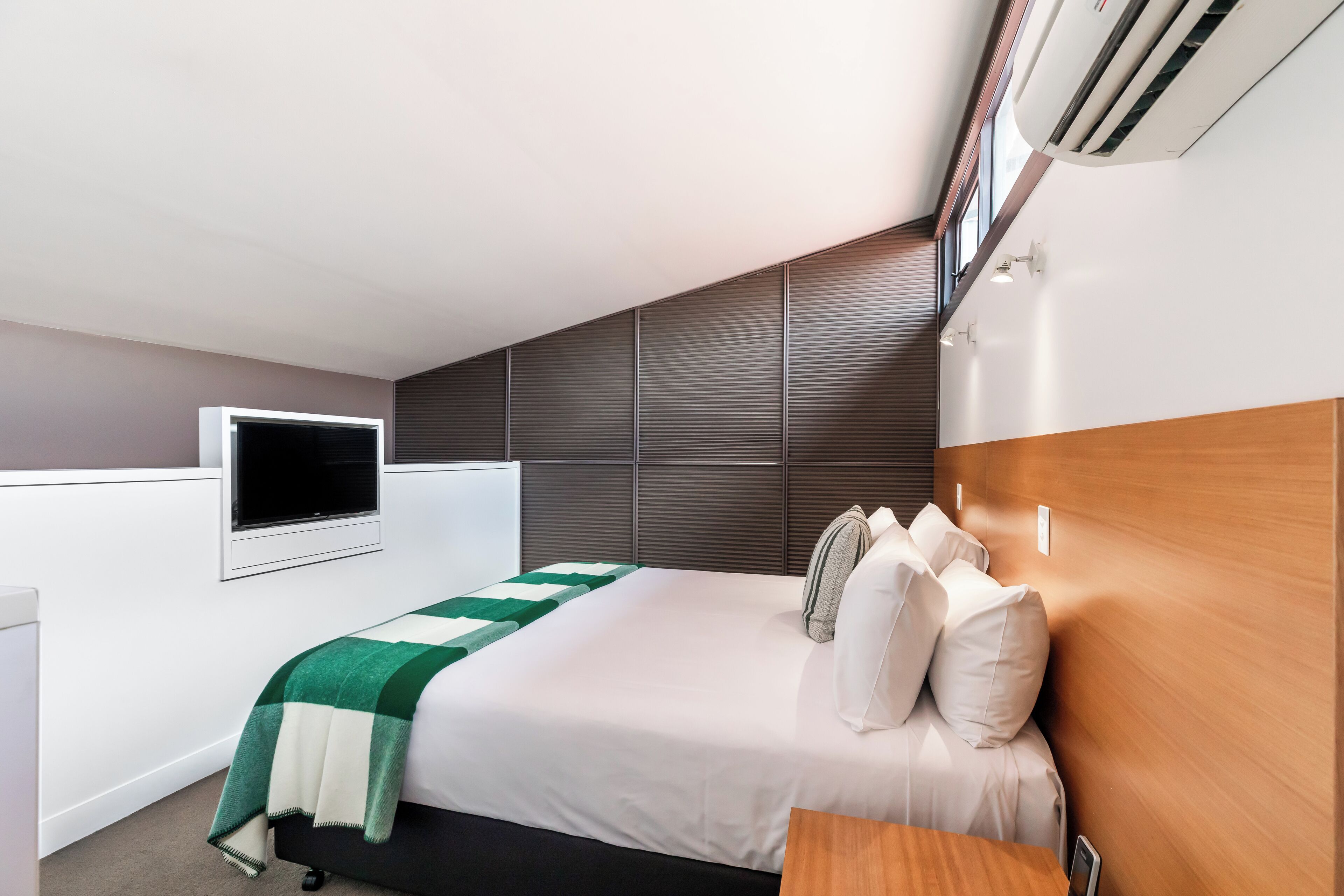 Ein modernes Hotelzimmer mit einem großen Bett, einem flachbildfernseher an der Wand und einer Klimaanlage über dem Bett.