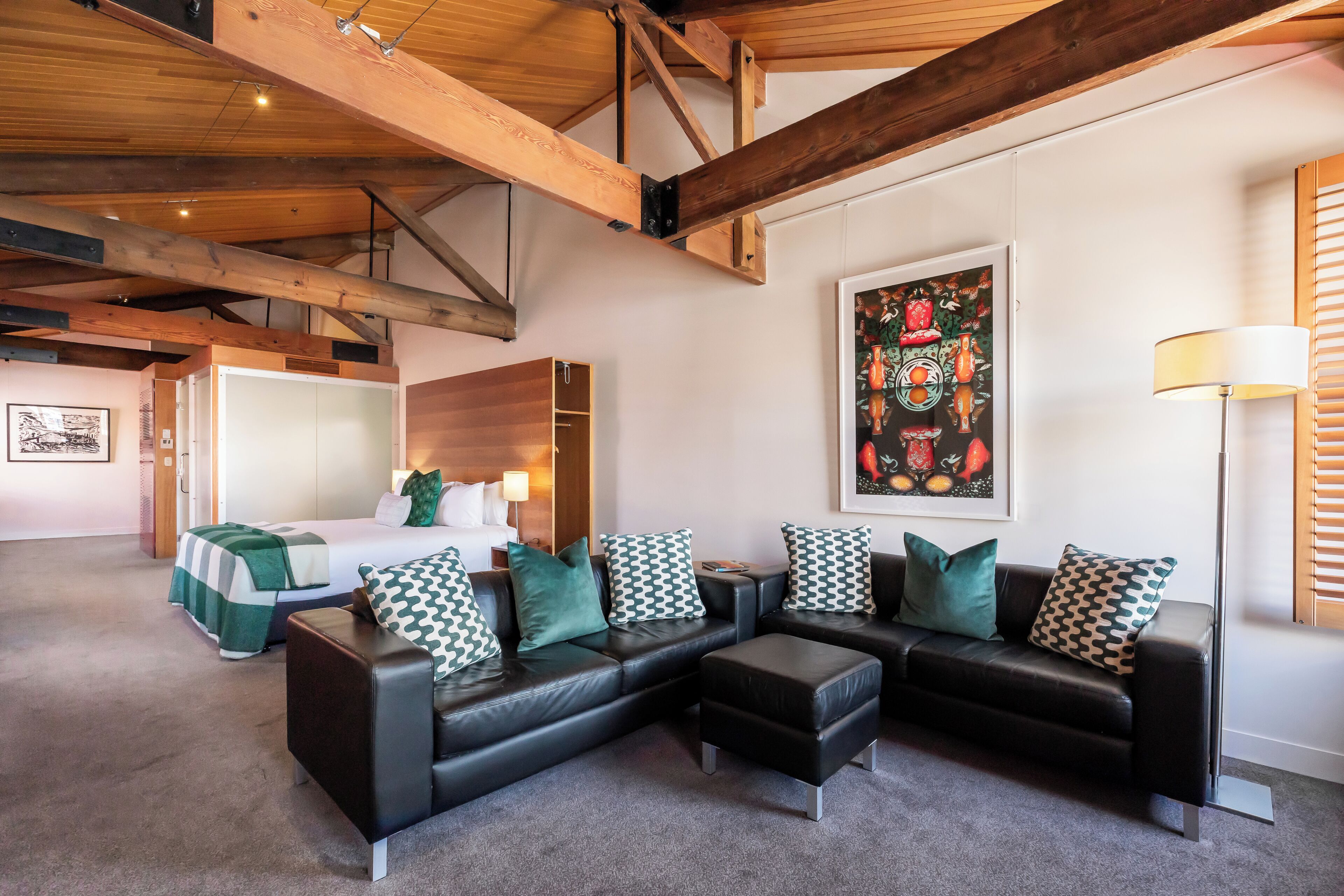 A modern hotel room with a sectional sofa, a bed, a desk, and a large painting.