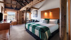 Een ruime slaapkamer met een groot bed, een houten hoofdbord en uitzicht op de stad door grote ramen.