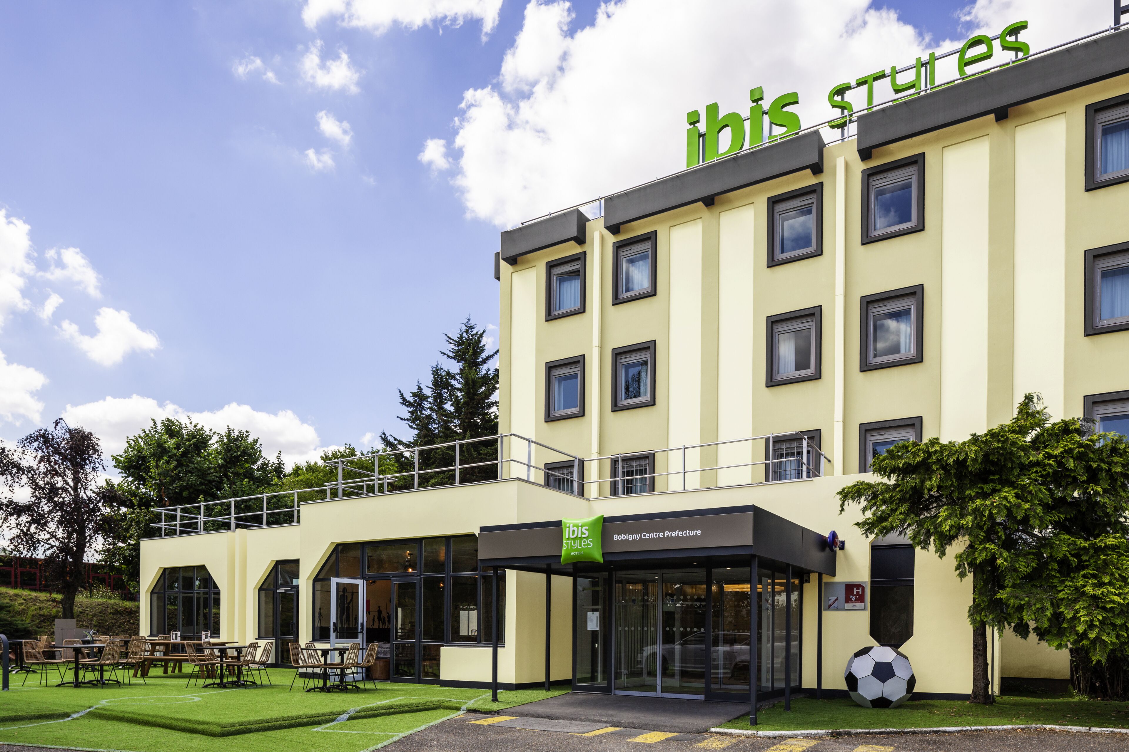 A hotel with a modern design, featuring a prominent "ibis styles" sign, a Bobigny Centre Prefecture label, and a visible entrance with a glass door.