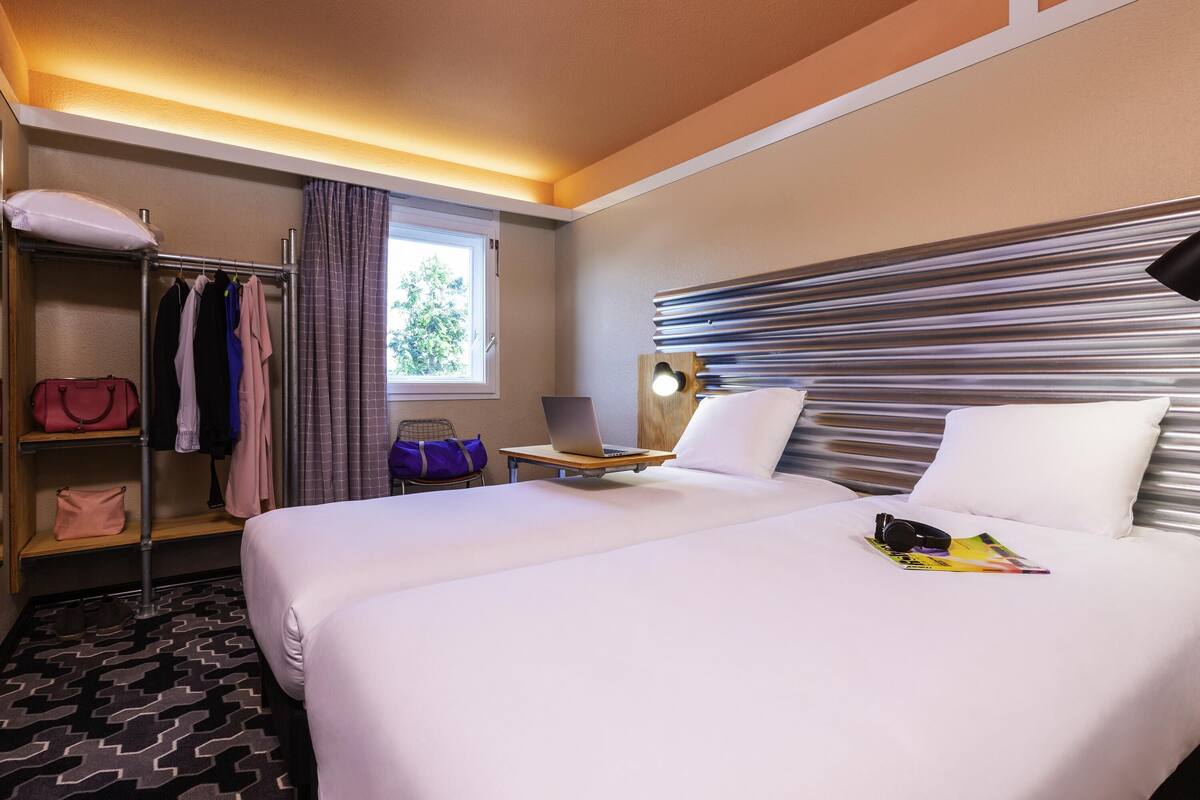 A hotel room with a bed, a desk with a laptop, a wardrobe, and a window with curtains.