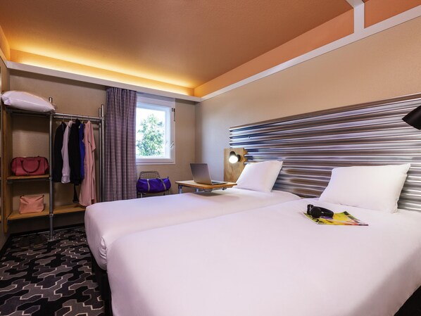 A hotel room with a bed, a desk with a laptop, a wardrobe, and a window with curtains.