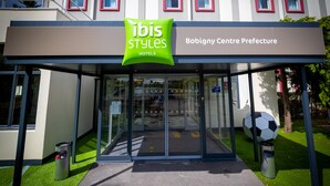La entrada a Bobigny Centre Prefecture Hotels, con una puerta de vidrio, un letrero verde en la parte superior y una escultura de balón de fútbol a la derecha.