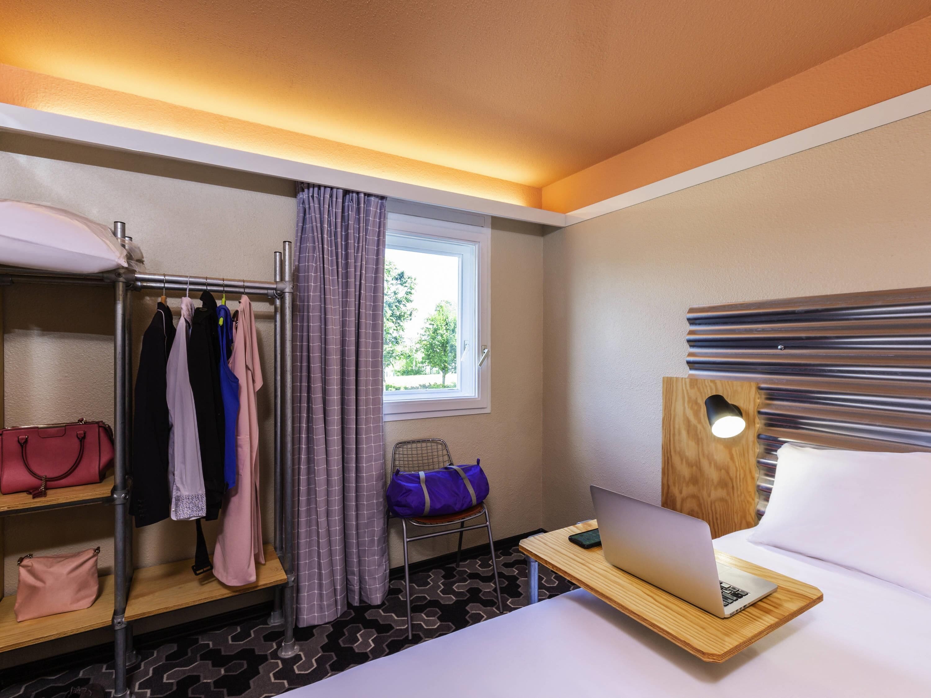 A hotel room with a bunk bed, a desk with a laptop, a window with curtains, and a bed with a pillow.