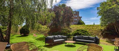 A well-maintained outdoor seating area with wicker chairs and sofas, a wooden table, and a grassy lawn.