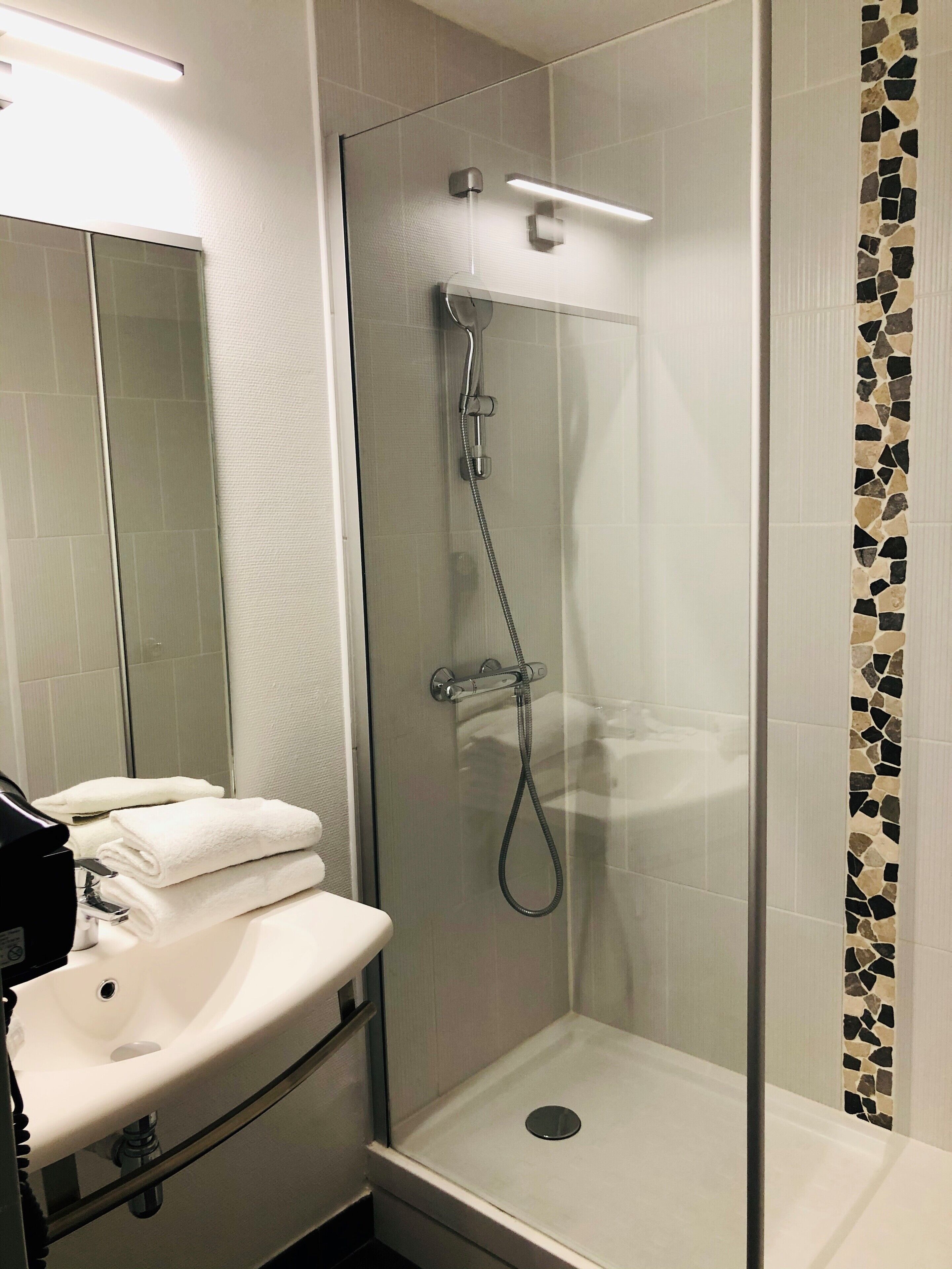Un baño moderno con ducha de vidrio, un lavabo blanco y un espejo.