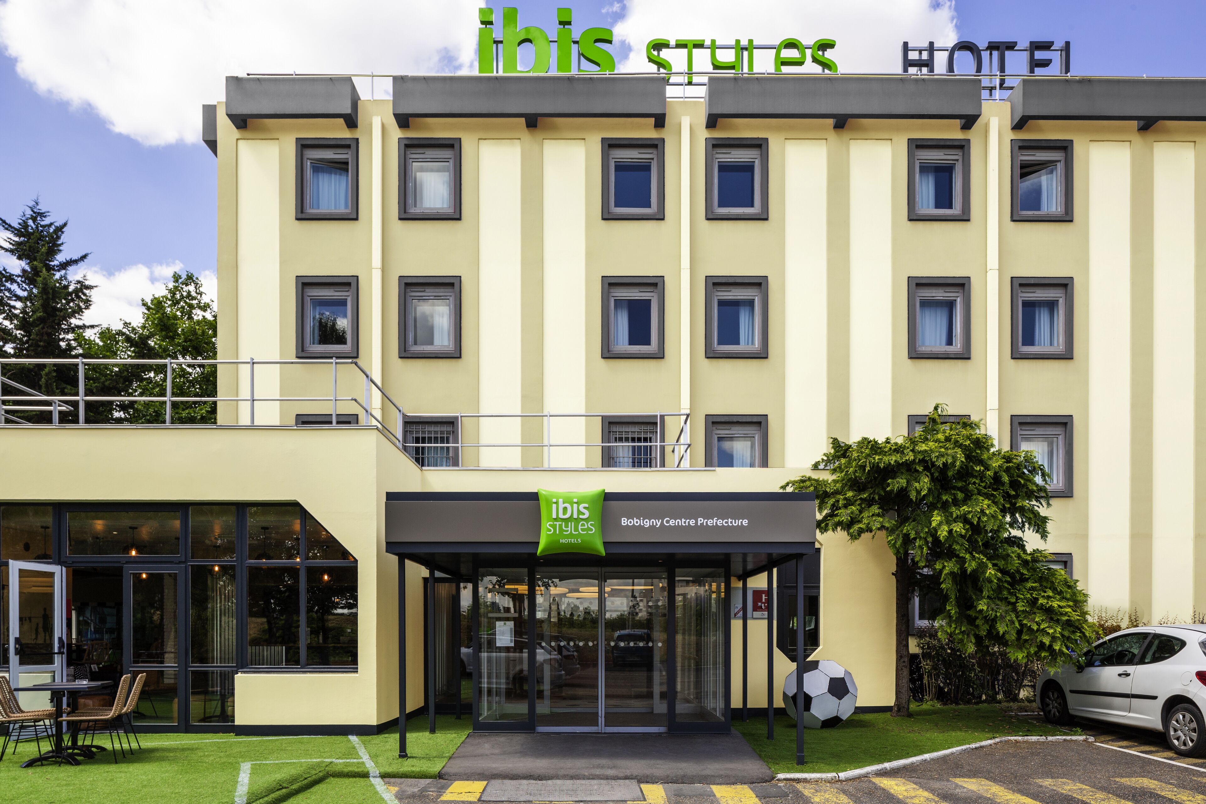 A hotel with a modern design, featuring a prominent "ibis Styles Hotel" sign, a Bobigny Centre Prefecture label, and a visible parking area.