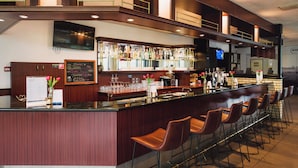 Una zona de bar con una barra alargada, varios taburetes y una gran variedad de botellas y copas.