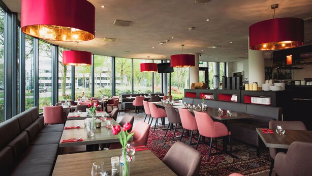 Un restaurante con varias mesas, sillas rojas y grandes lámparas colgantes rojas.