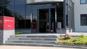 Una entrada de hotel moderna con fachada de vidrio, un letrero que dice "Bastion Hotel" y una escalera que conduce a la entrada.