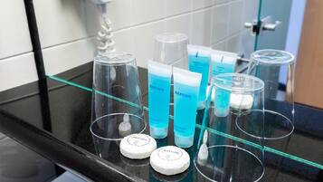 En badeværelsesbordplade med diverse toiletartikler, heriblandt en hårtørrer, et glas og flere flasker Bastian shampoo.