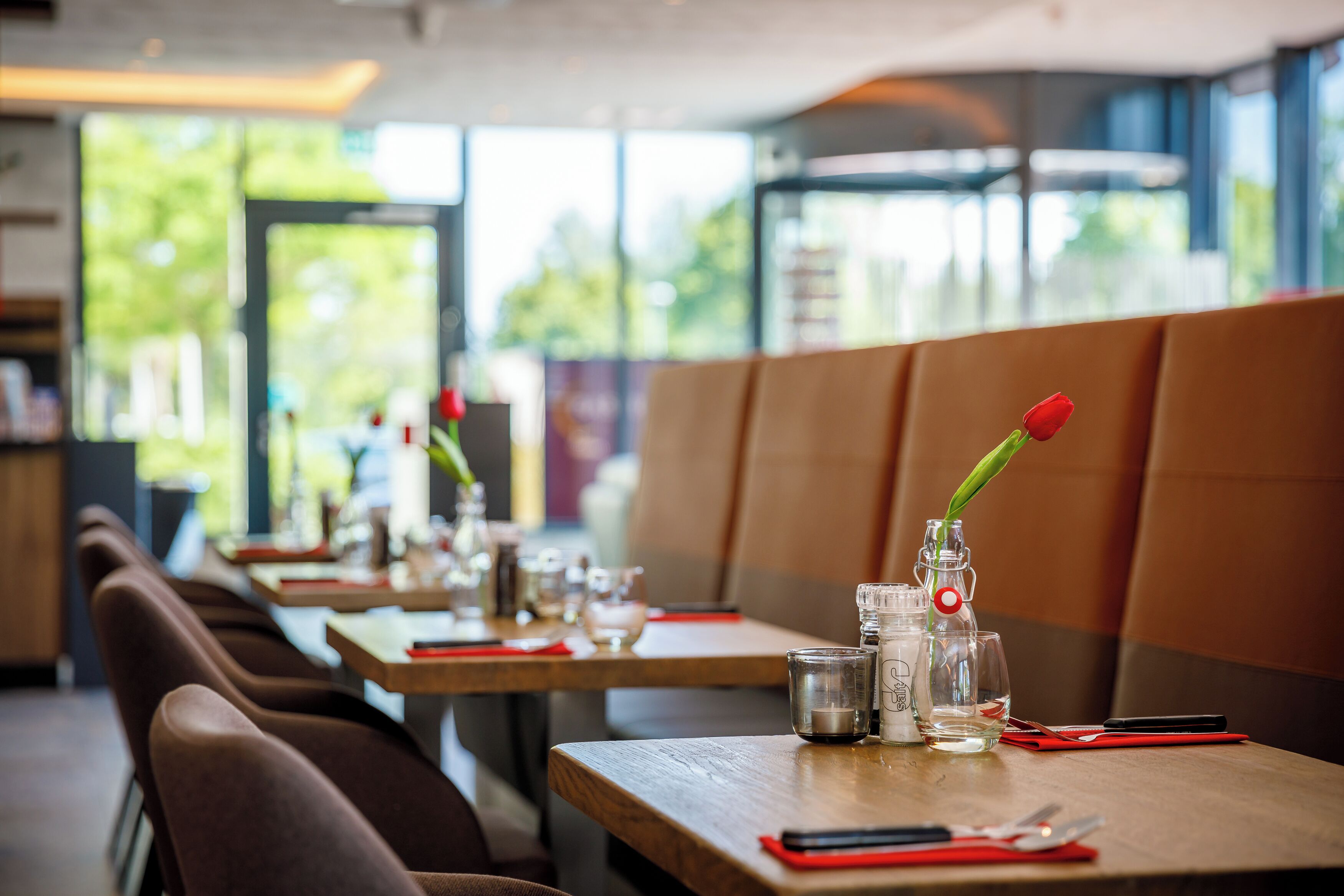 A restaurant with wooden tables, clear glassware, and a single red rose in a bottle.
