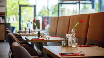 Ein Restaurant mit Holztischen, klarem Glasgeschirr und einer roten Rose in einer Flasche.