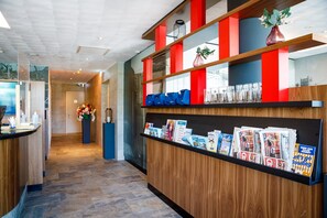 A reception area with a wooden counter, magazines, and a vase with flowers. - Bastion Hotel Haarlem Velsen (Santpoort-Noord)