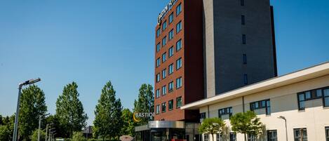 A modern hotel with a prominent sign, a parking area, and a clear sky.