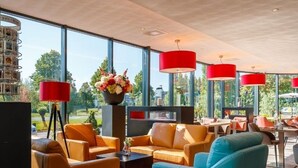 A modern lounge area with orange and blue seating, a red lamp, and a large window offering a city view.