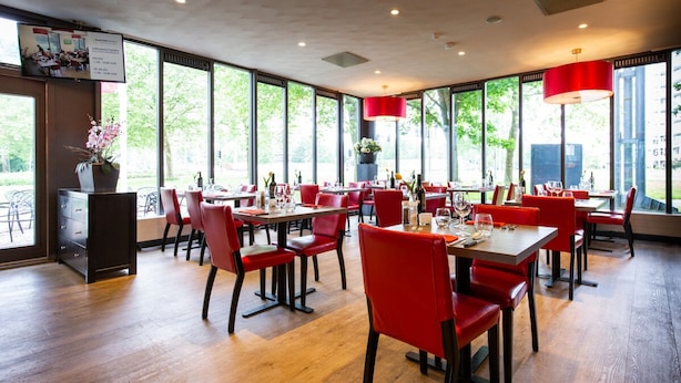 A restaurant with red chairs and tables, large windows, and a wooden floor.