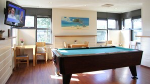 A pool table in a room with a television, a painting, and a window with a view of trees.
