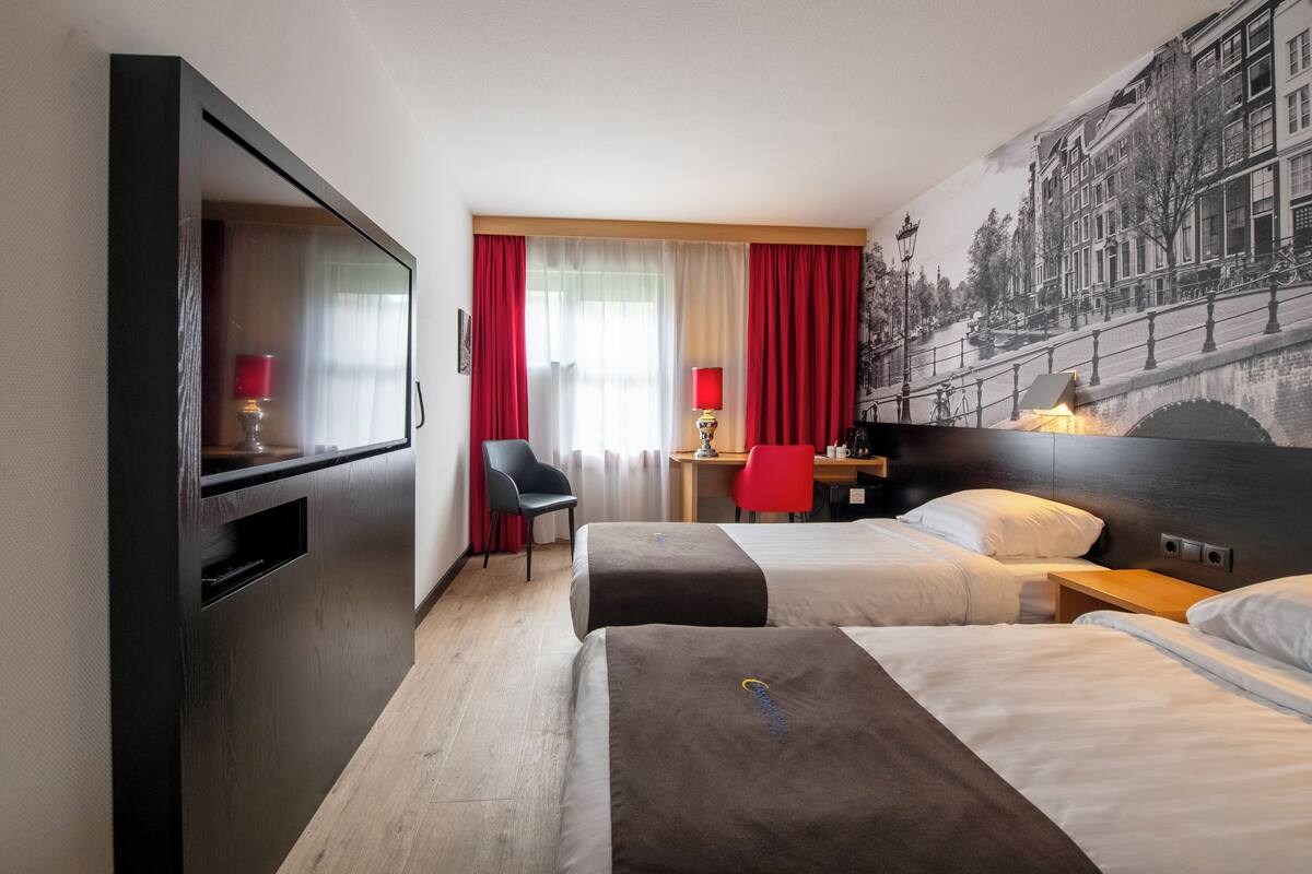 Hotellihuone, jossa on kaksi sänkyä, työpöytä, tuoli ja televisio.
