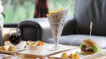 Ein Esstisch mit einem Burger, Pommes in einer Zeitungsrolle, einem Glas Rotwein und einer Schüssel Suppe.