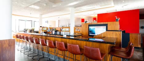 A modern bar area with a long counter, multiple stools, and a large screen.